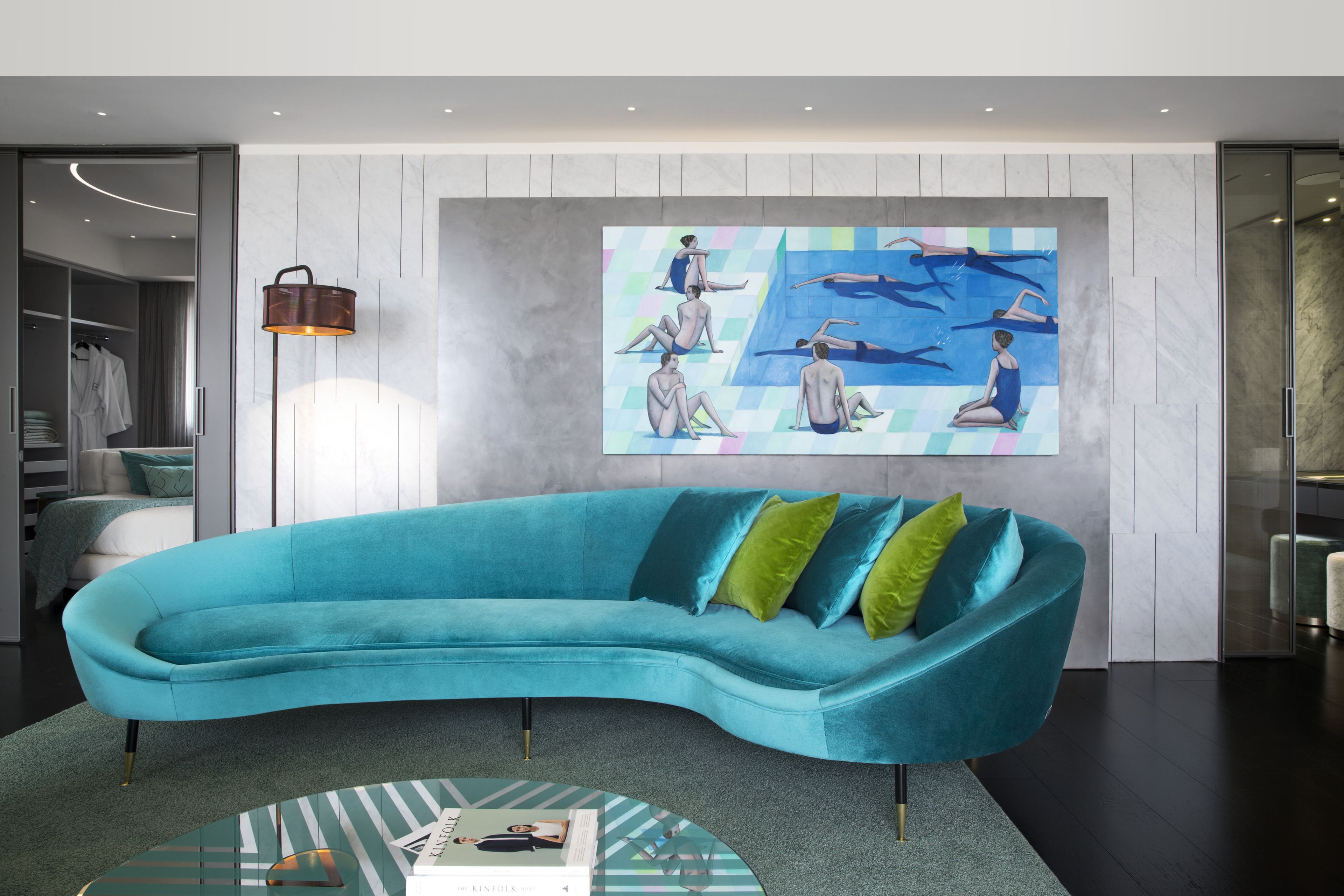 A modern living room with a teal sofa, a glass coffee table, and a large abstract painting on the wall.