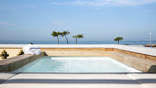 Piscina infinita no terraço com deck de madeira e vista para o oceano.