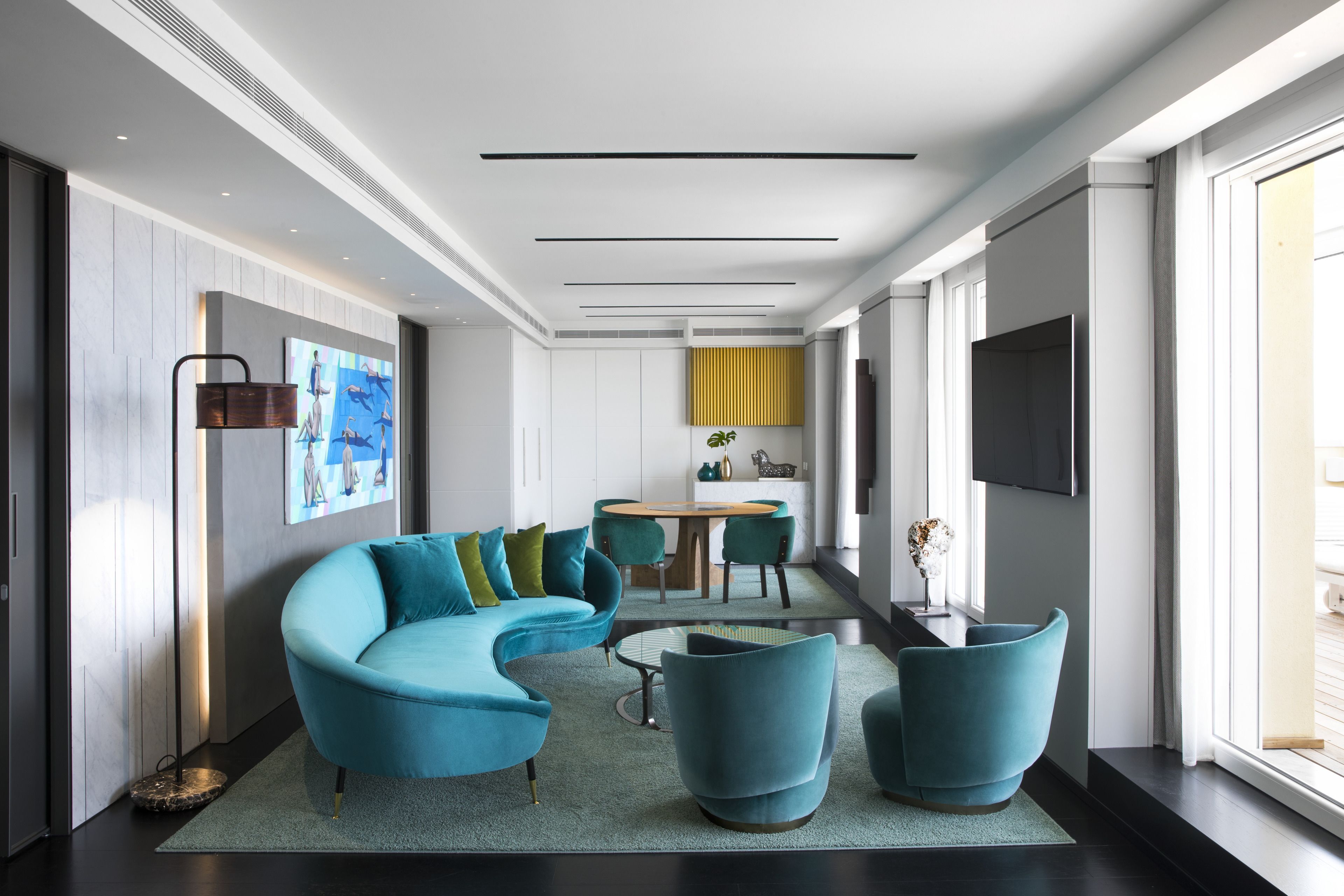 Ein modernes Wohnzimmer mit einer gebogenen Couch, Türkis-farbenen Sessel, einem Couchtisch und einem Essbereich mit rundem Tisch und Stühlen.