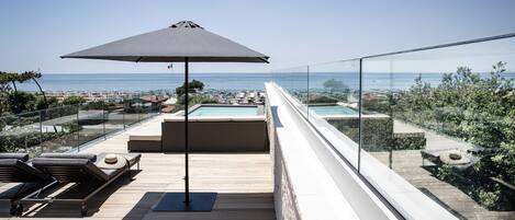 Una terraza en la azotea con piscina, sillas de descanso y vistas al mar.