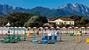 Uma praia com cadeiras e guarda-sóis de praia, uma fileira de cabanas coloridas e um prédio com telhado vermelho.
