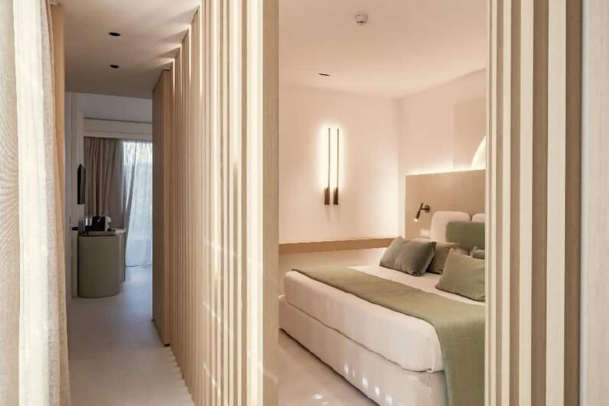 A modern hotel room with a bed, bedside table, and a wall-mounted light fixture.