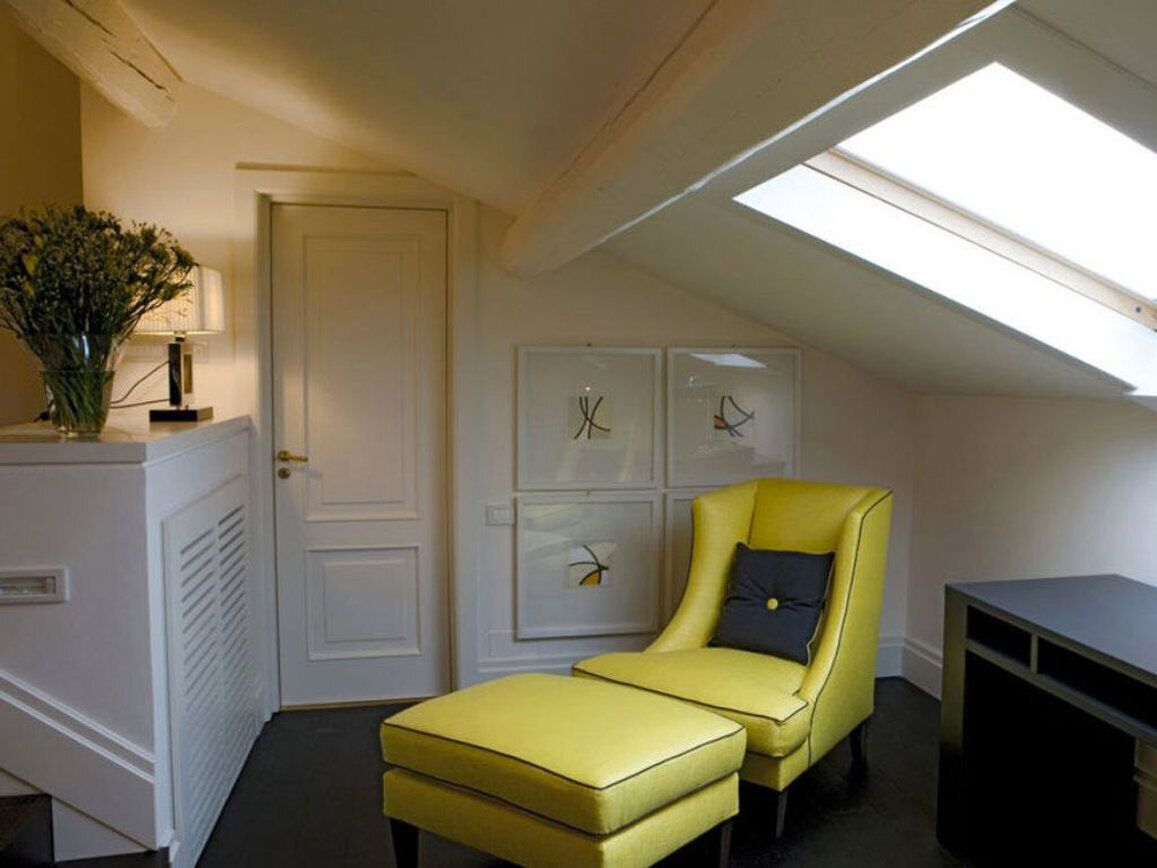 A room with a yellow armchair and ottoman, a white door, and framed artwork on the wall.