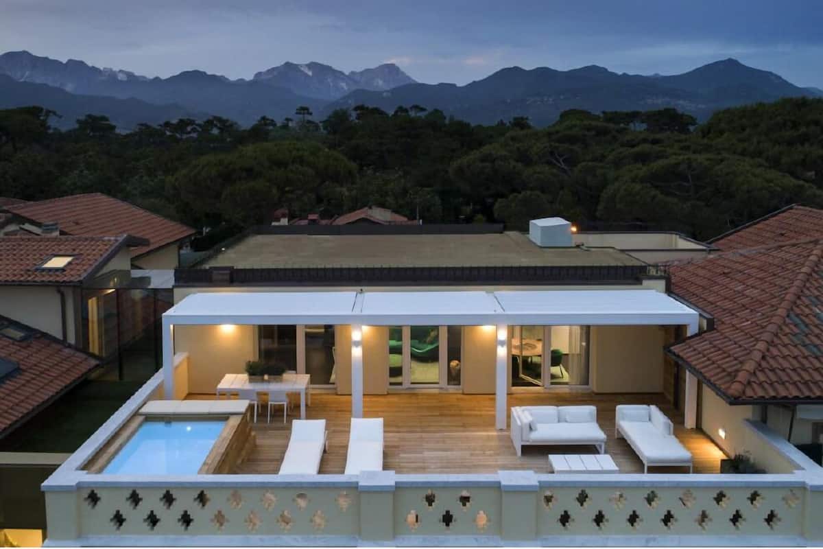 A modern house with a rooftop pool, outdoor seating, and a view of mountains.