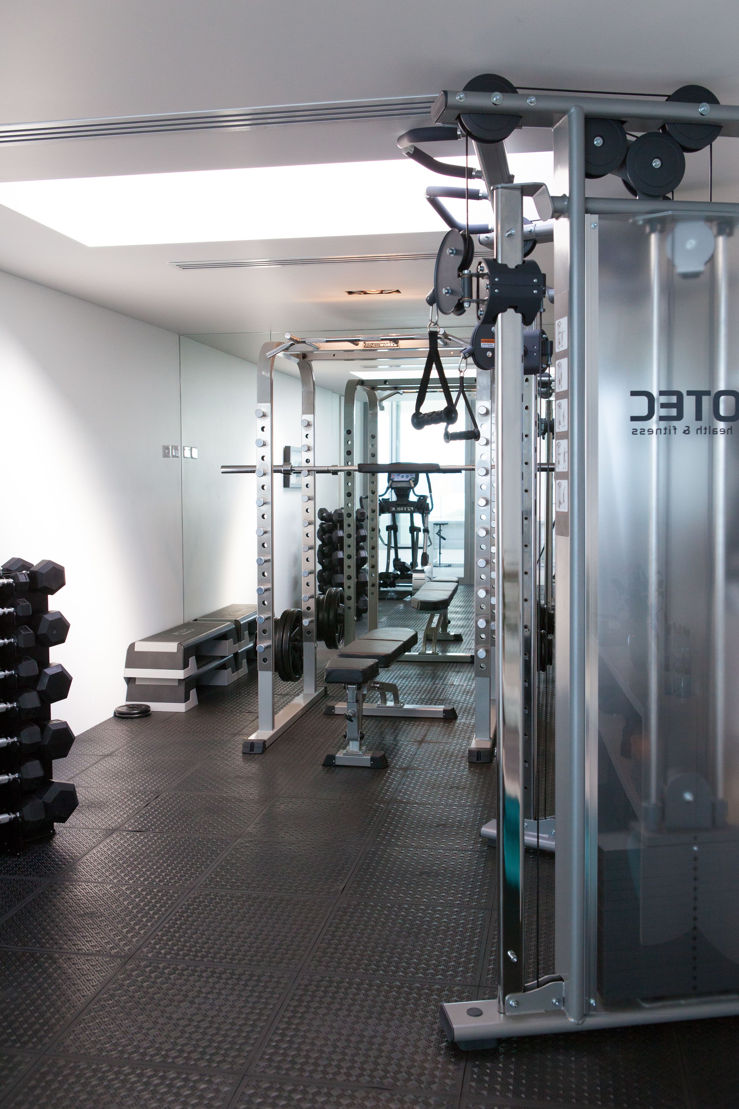 A gym with weightlifting equipment, benches, and a mirrored wall.