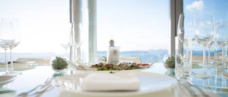 A table set for a meal with wine glasses, a bottle of wine, and a view of the ocean.