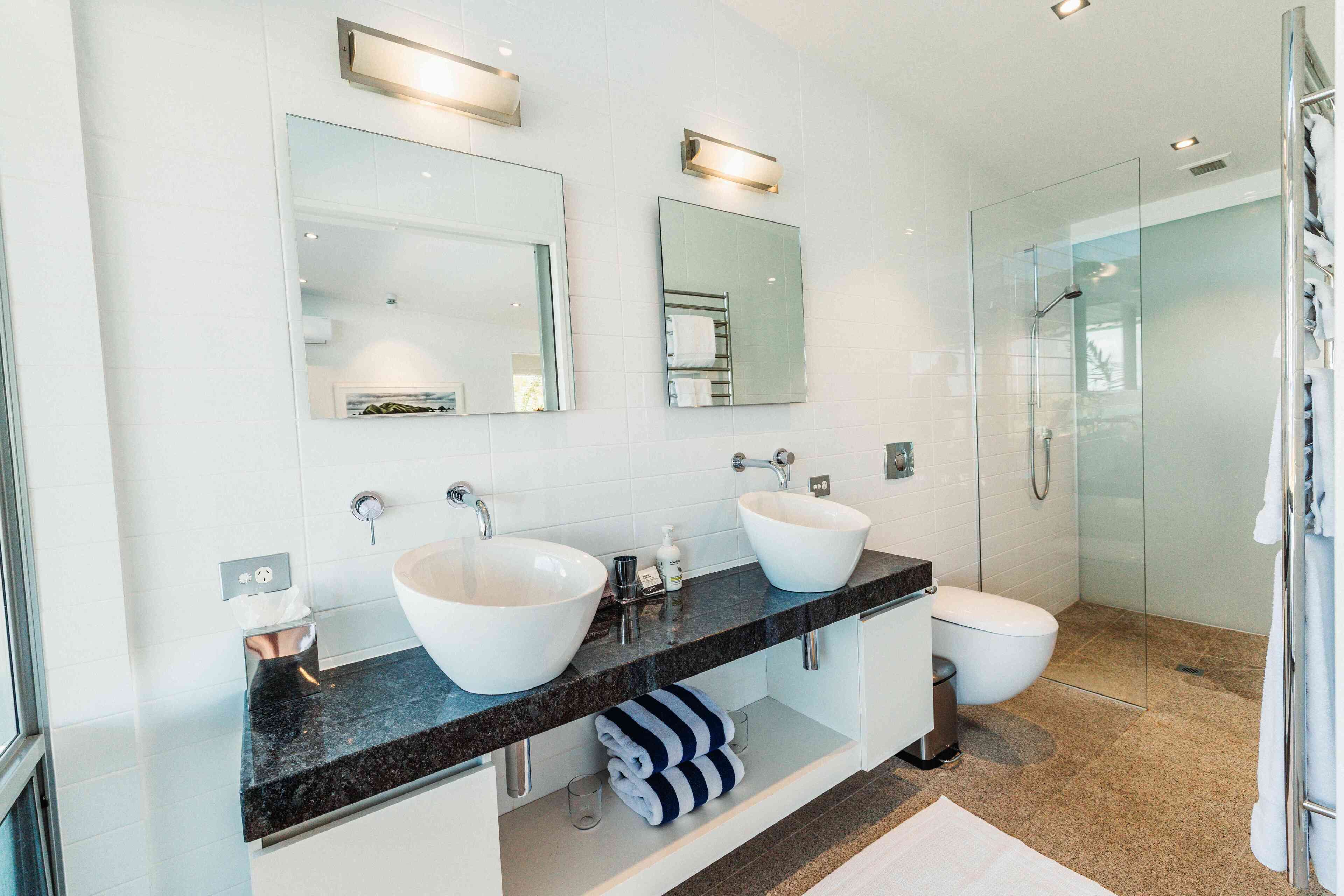 A modern bathroom with two large white sinks, a glass shower enclosure, and a white toilet.