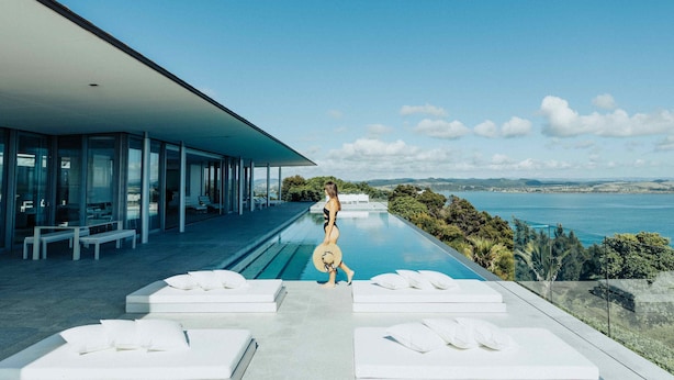 A modern pool area with a view of the sea, outdoor seating, and a glass-enclosed building. - Eagles Nest (Russell)