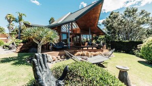 A modern house with a sloped roof, large windows, and a deck with outdoor furniture. - Eagles Nest (Russell)