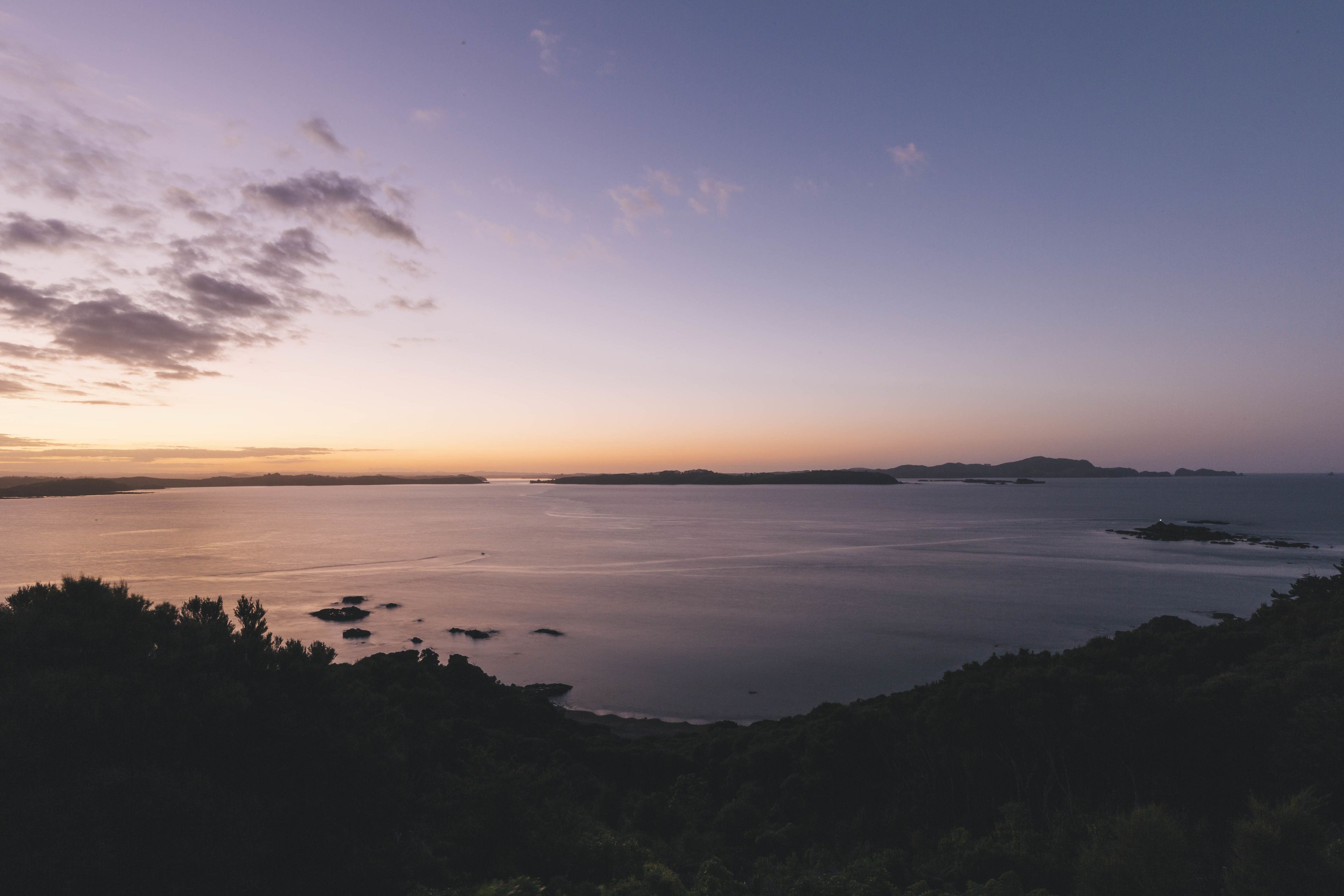 Un paysage côtier avec une mer calme, des reliefs lointains et un ciel dégagé.