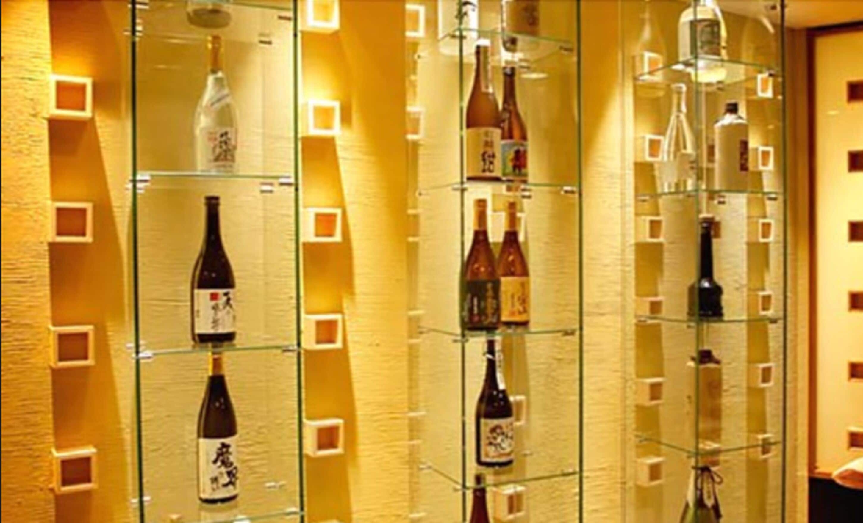 Una variedad de botellas, presumiblemente bebidas alcohólicas, dispuestas en estantes dentro de una habitación bien iluminada con una pared con textura.