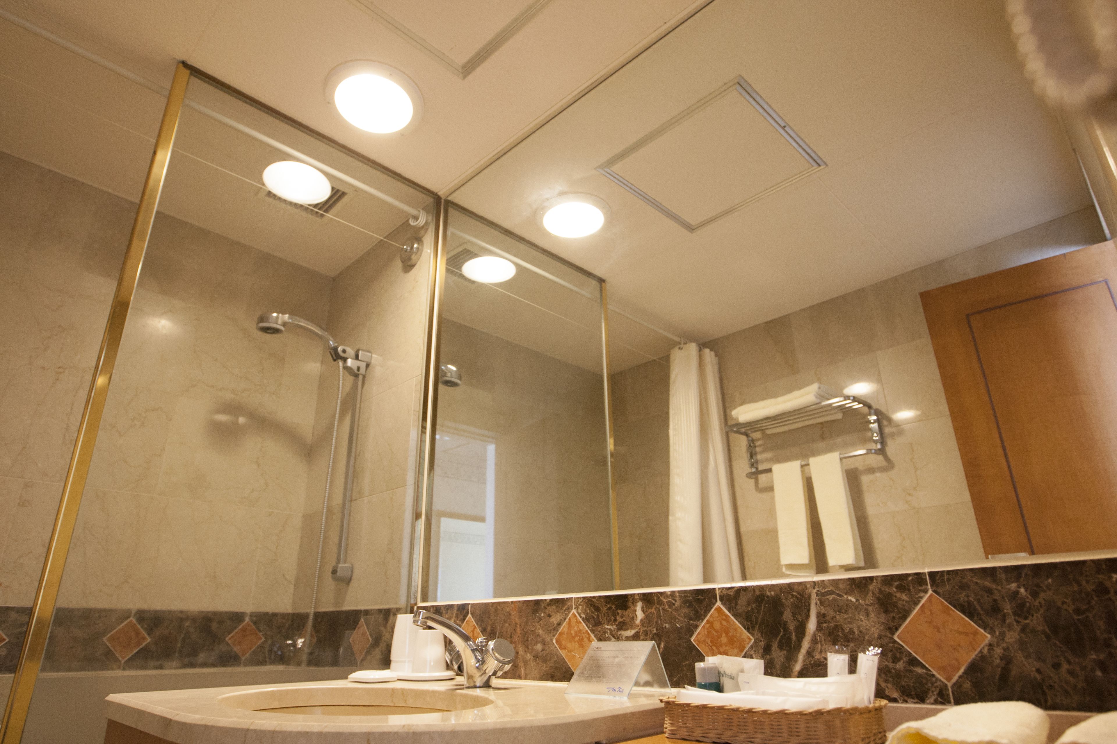 A bathroom with a large mirror, a shower, a sink, and a towel rack.