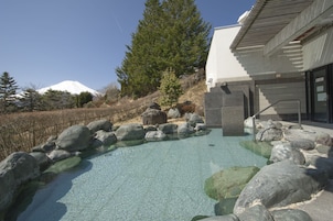 Una piscina exterior cristalina con rocas, un edificio moderno con techo inclinado y una montaña nevada al fondo.