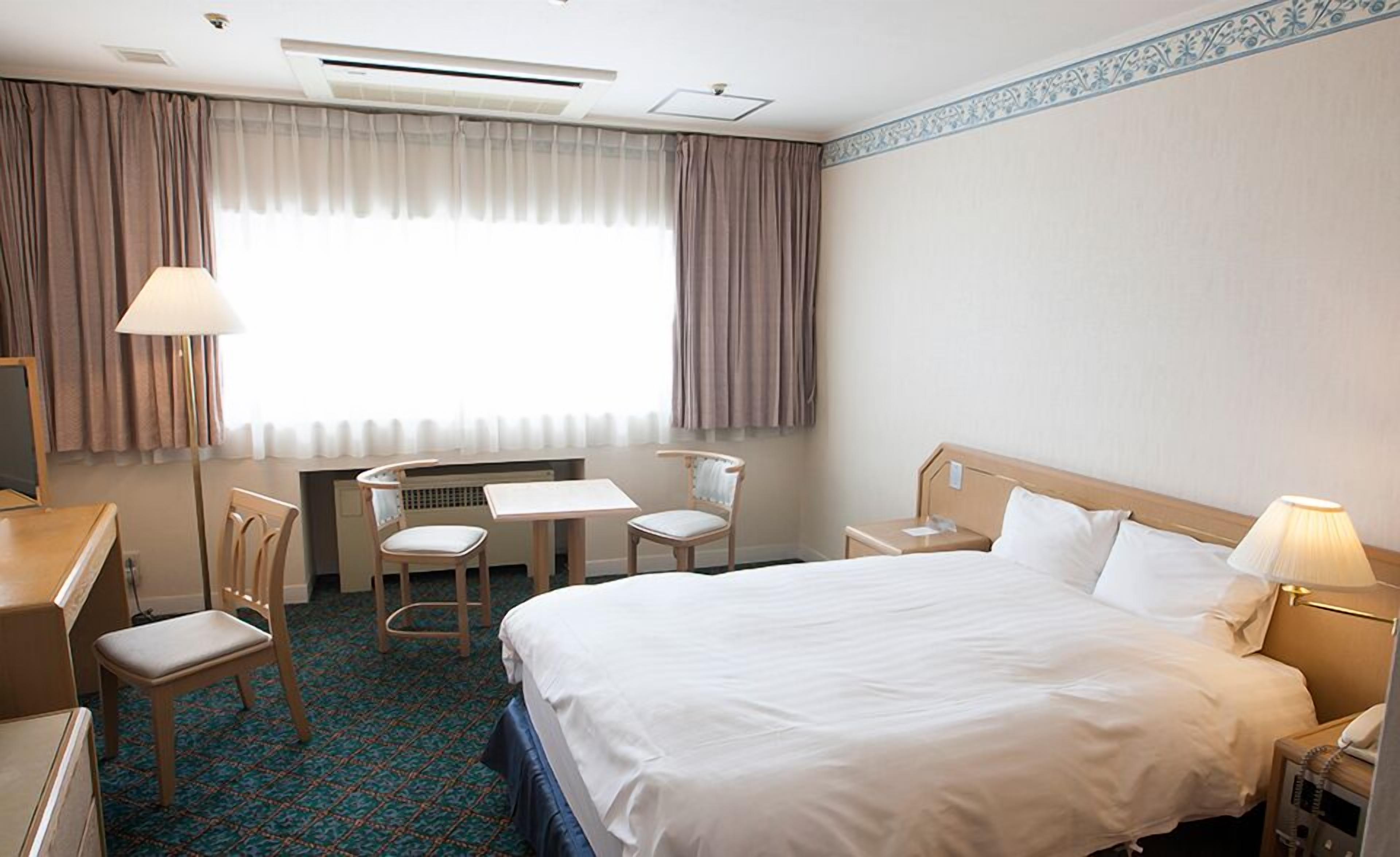 A hotel room with a bed, desk, chairs, and a window with curtains.