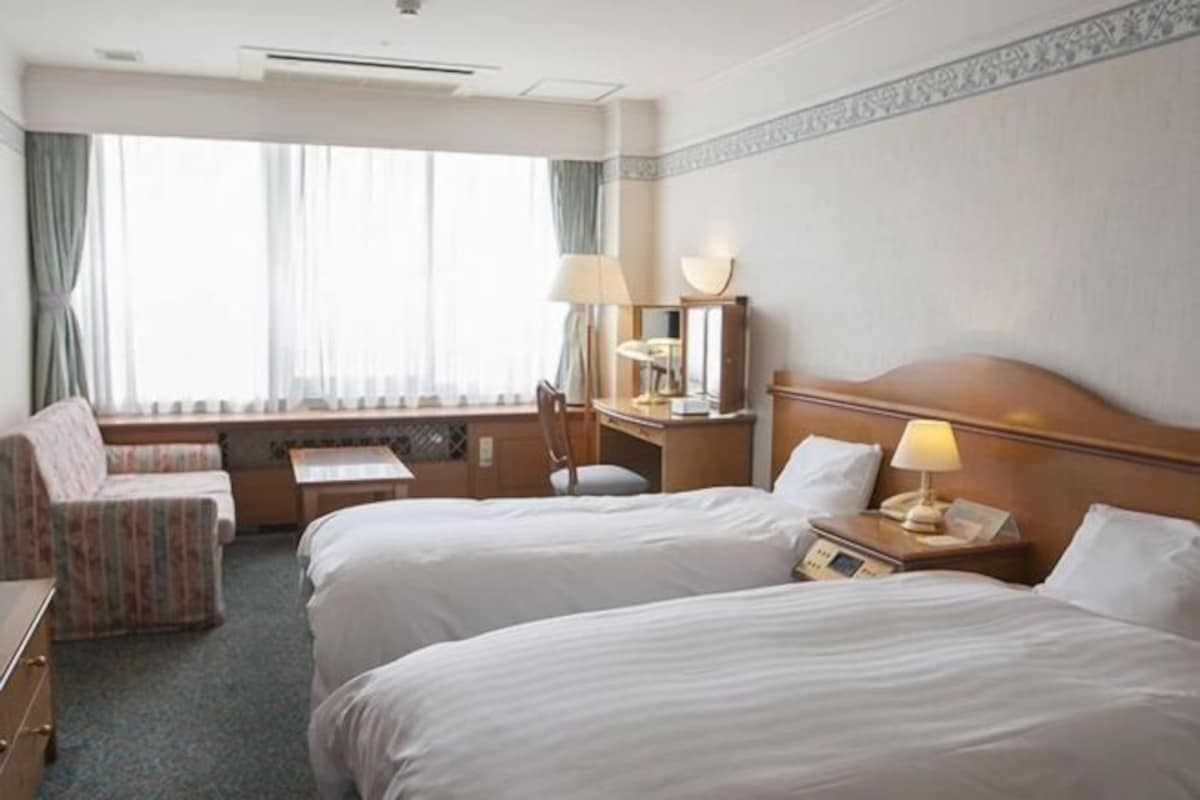 A hotel room with two beds, a desk, a chair, and a window with curtains.