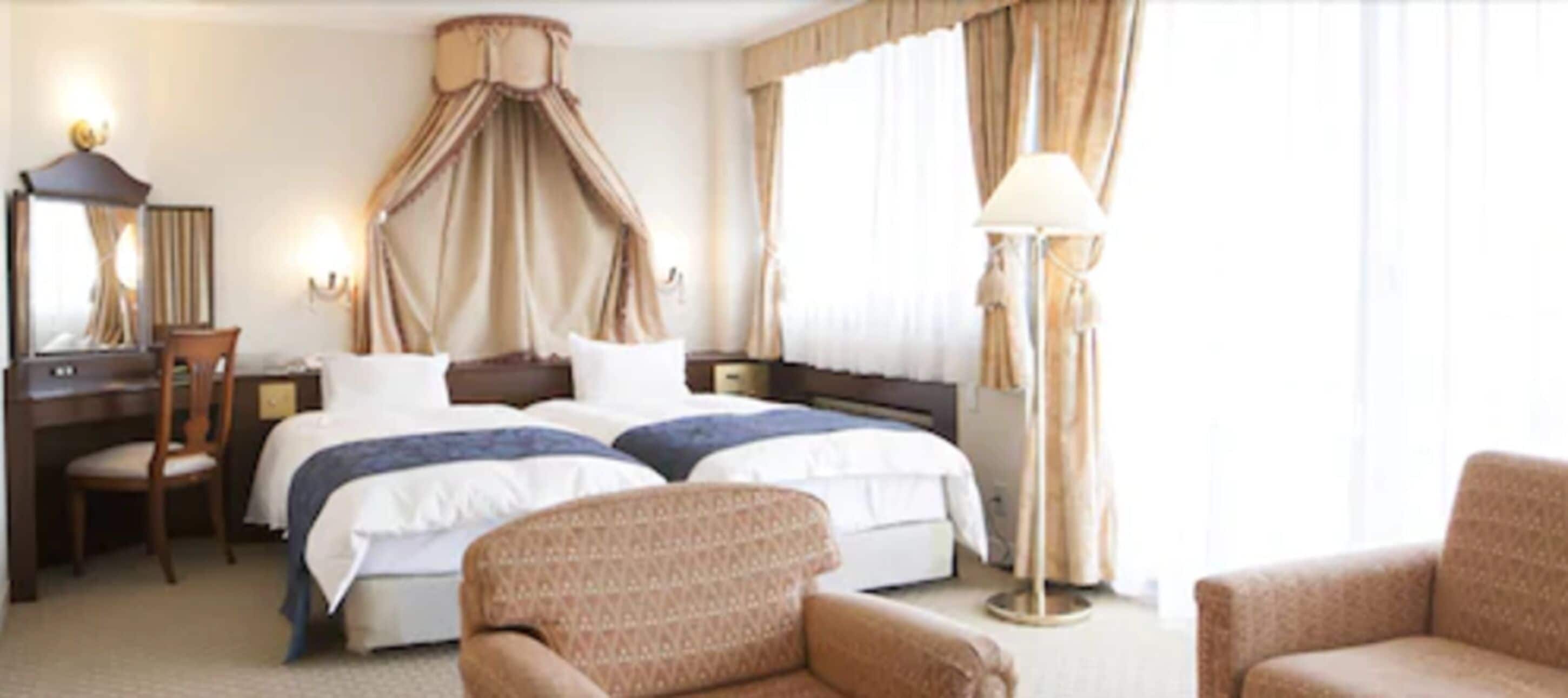 A hotel room with a large bed, a desk, a chair, and a floor lamp.