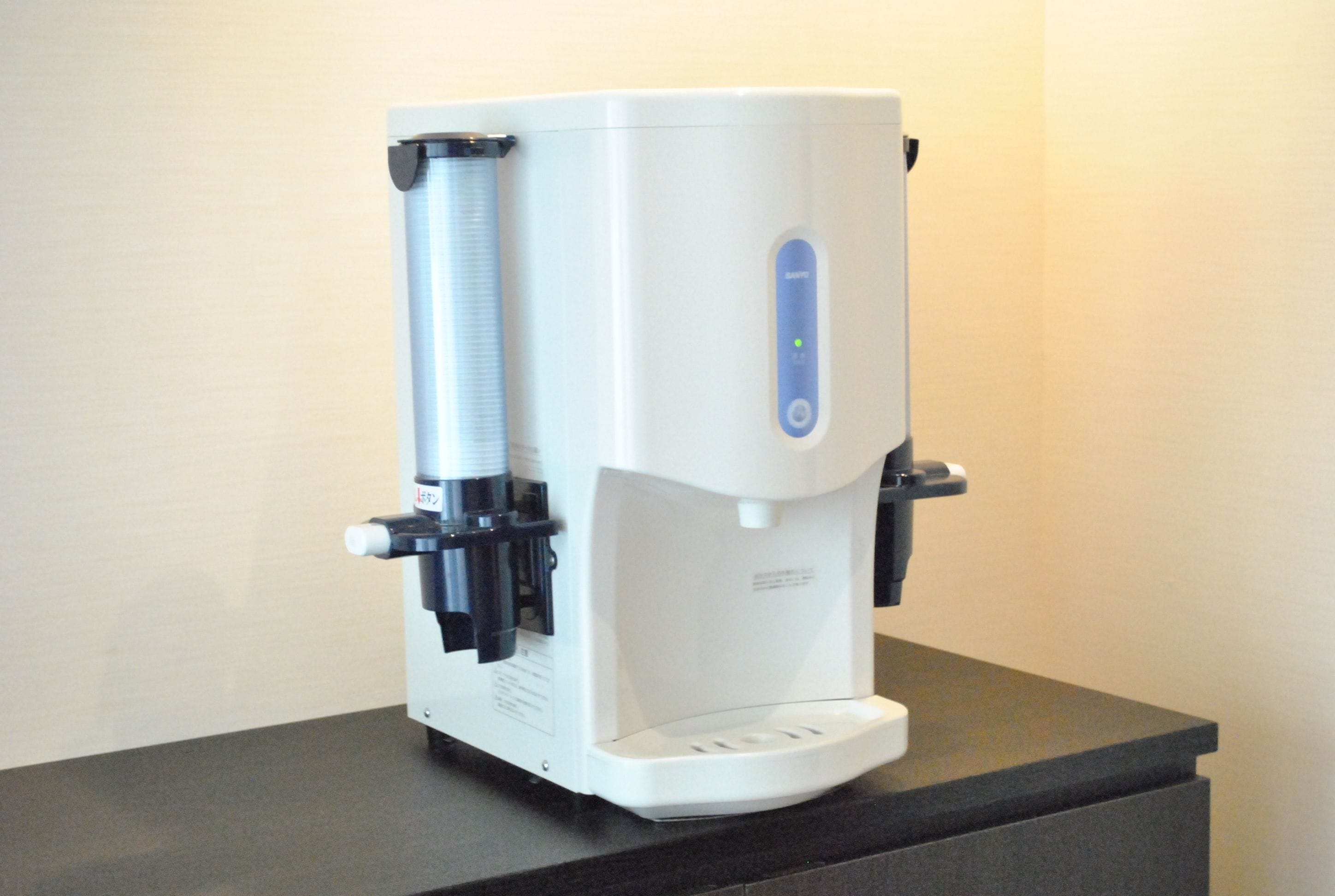 Una máquina de café con dispensador de agua y panel de botones, sobre una encimera oscura.