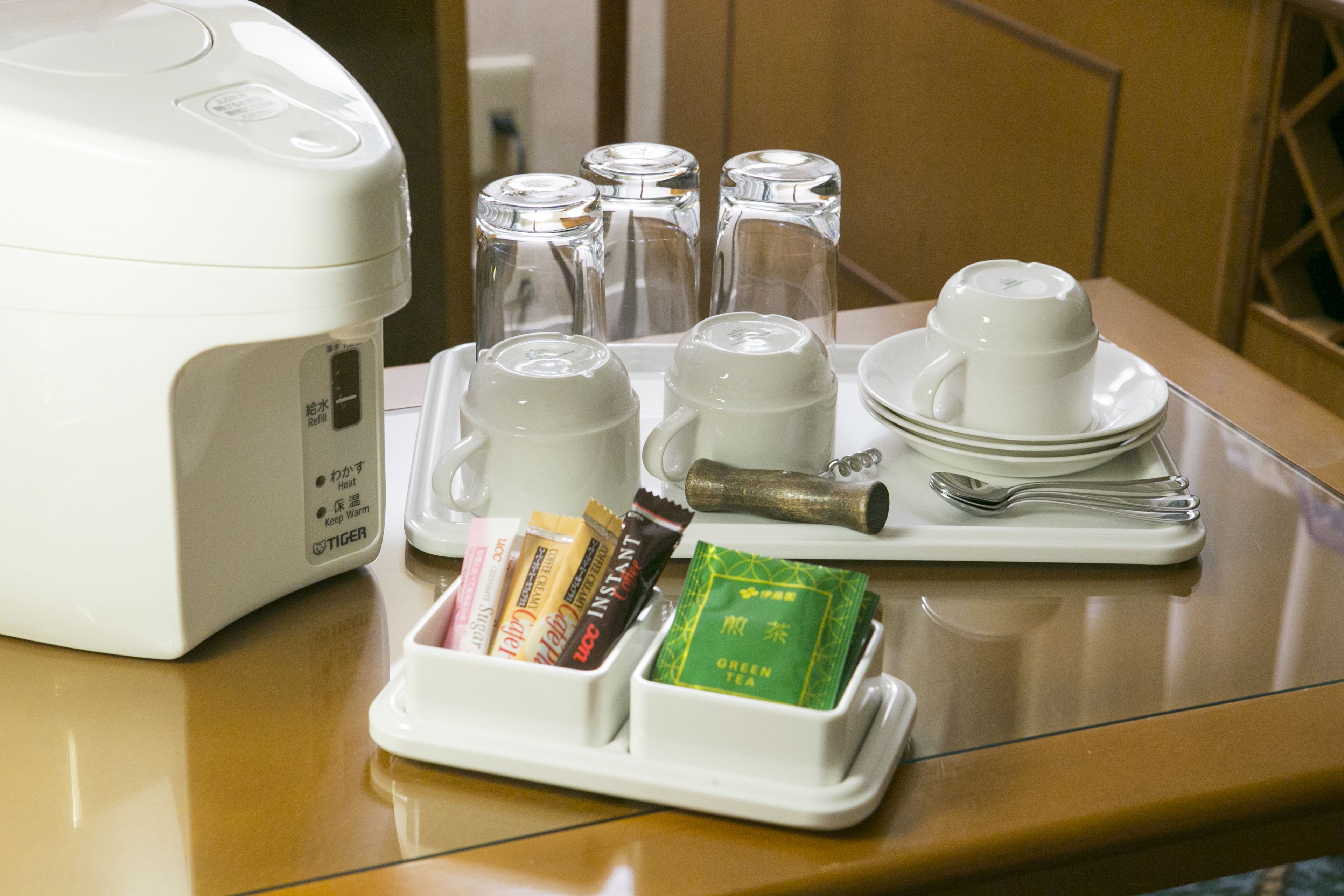 A table with a white electric kettle, four glass cups, a tea set, and a tray with tea bags and snacks.