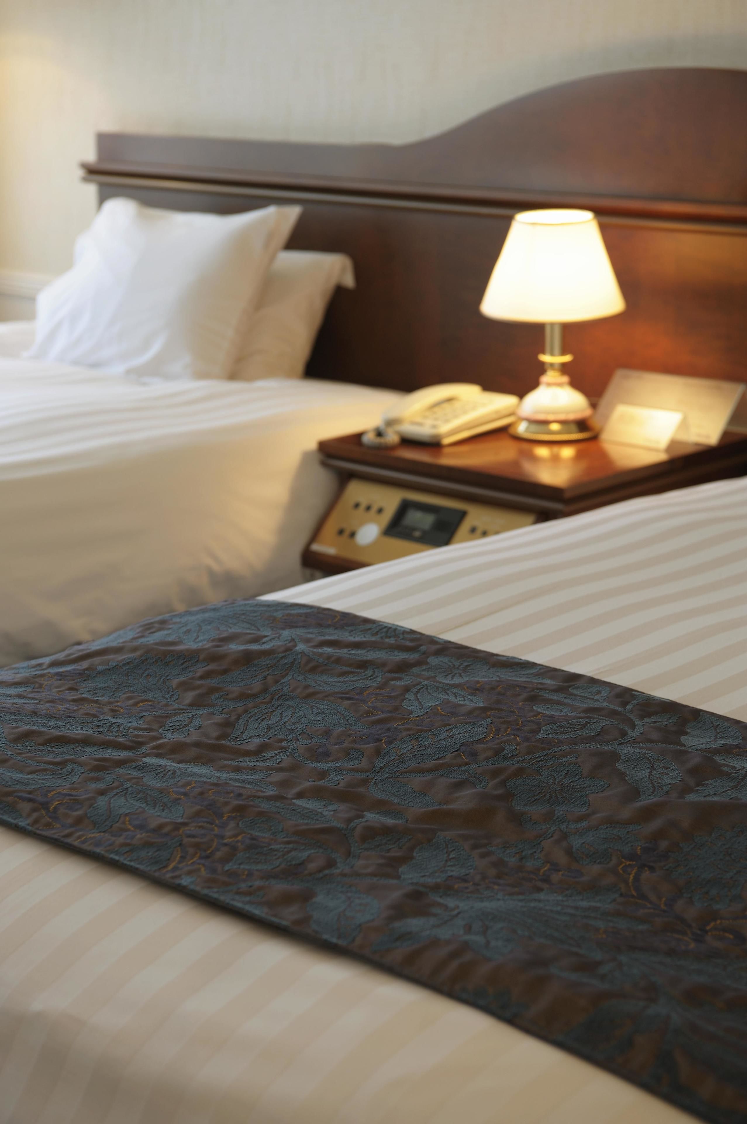 A hotel room with two beds, a nightstand with a lamp, a telephone, and a clock.