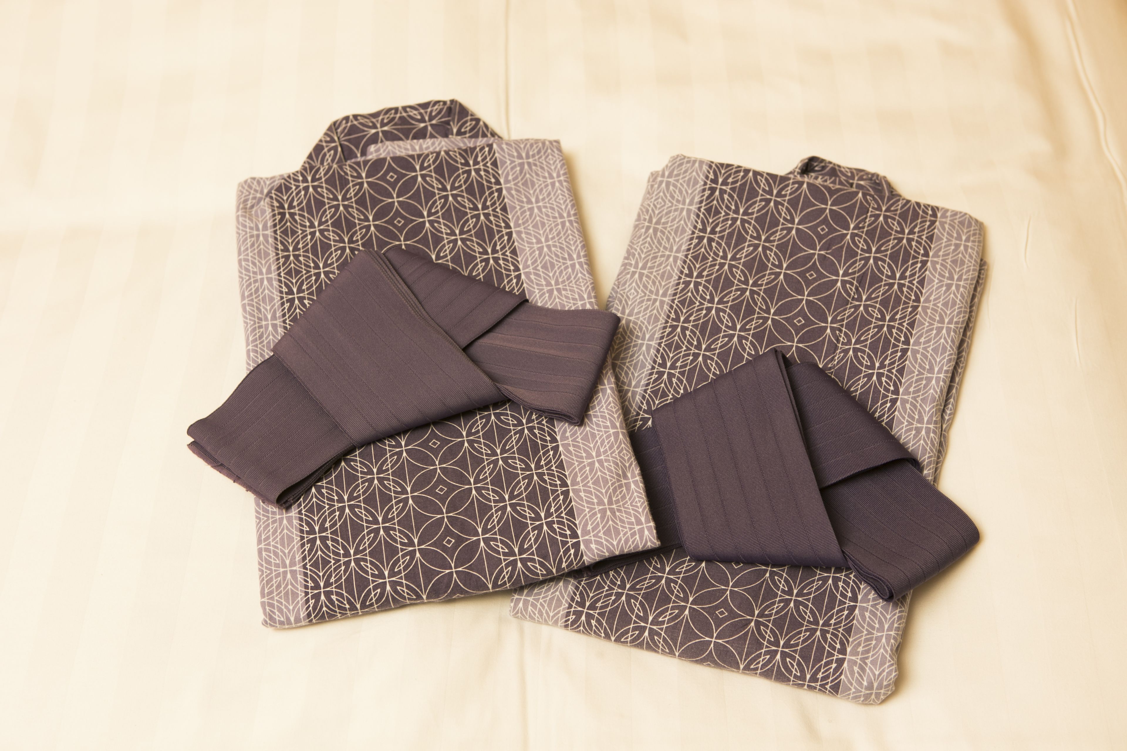 Twee netjes gevouwen kimonos met een geometrisch patroon op een bed.