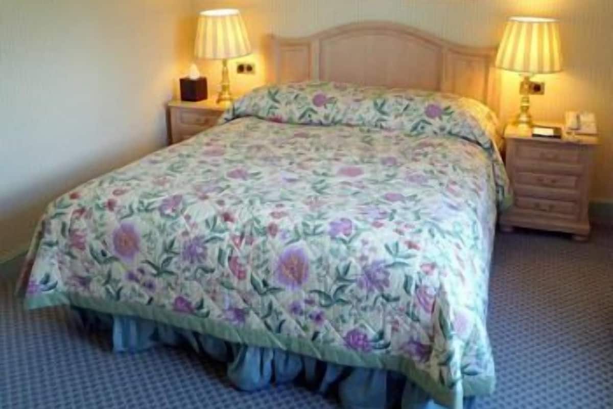 A neatly made bed with floral bedding, two bedside lamps, and two framed pictures on the wall.