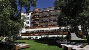 A multi-story hotel with outdoor seating areas and a well-maintained lawn. - Grand Hôtel du Golf & Palace (Crans-Montana)