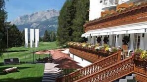 A hotel with a grand staircase, outdoor seating, and a view of mountains. - Grand Hôtel du Golf & Palace (Crans-Montana)