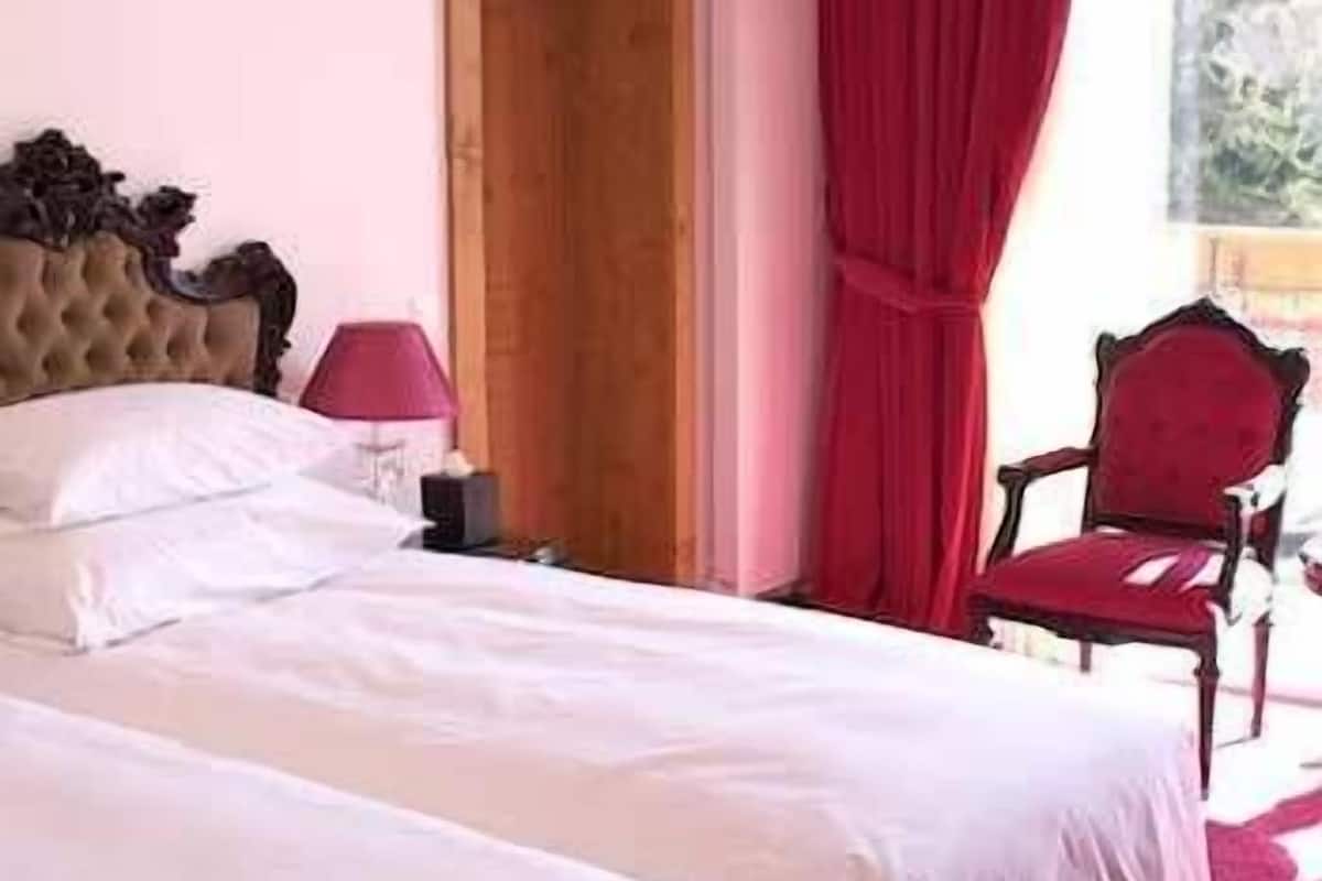 A bedroom with a bed, a nightstand, a lamp, a chair, and a wooden door.
