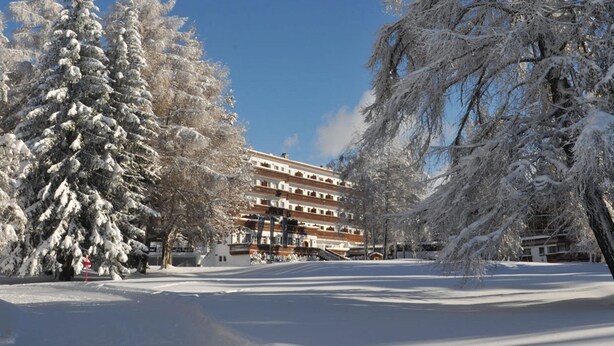 A snow-covered courtyard with a multi-story building featuring balconies and a central entrance. - Grand Hôtel du Golf & Palace (Crans-Montana)
