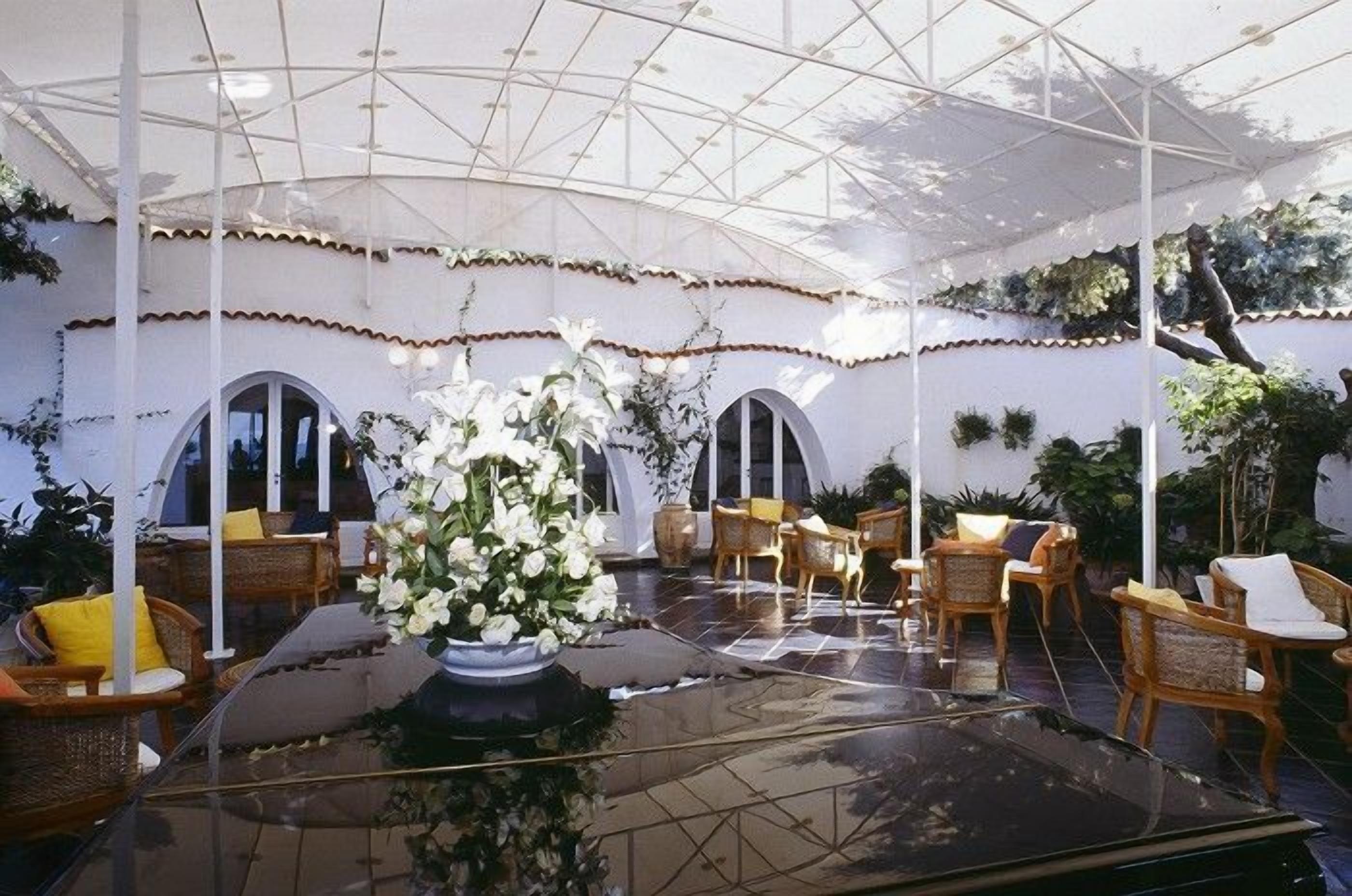 An outdoor patio area with a glass table, wicker chairs, and potted plants.