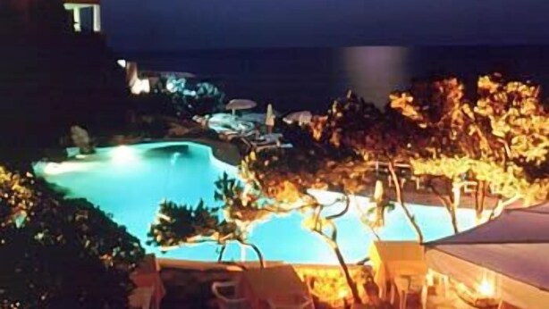 A nighttime view of a resort with a swimming pool, lounge chairs, and a building with illuminated windows. - Hotel Punta Rossa (San Felice Circeo)