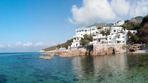 A coastal building with multiple white structures, clear blue water, and a rocky shoreline. - Hotel Punta Rossa (San Felice Circeo)