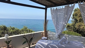 A bedroom with a view of the sea, a bed with white linens, a small table with a candle, and a chair. - Hotel Punta Rossa (San Felice Circeo)