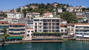 Et hotel ved vandet med flere etager, balkoner og udendørs siddepladser.