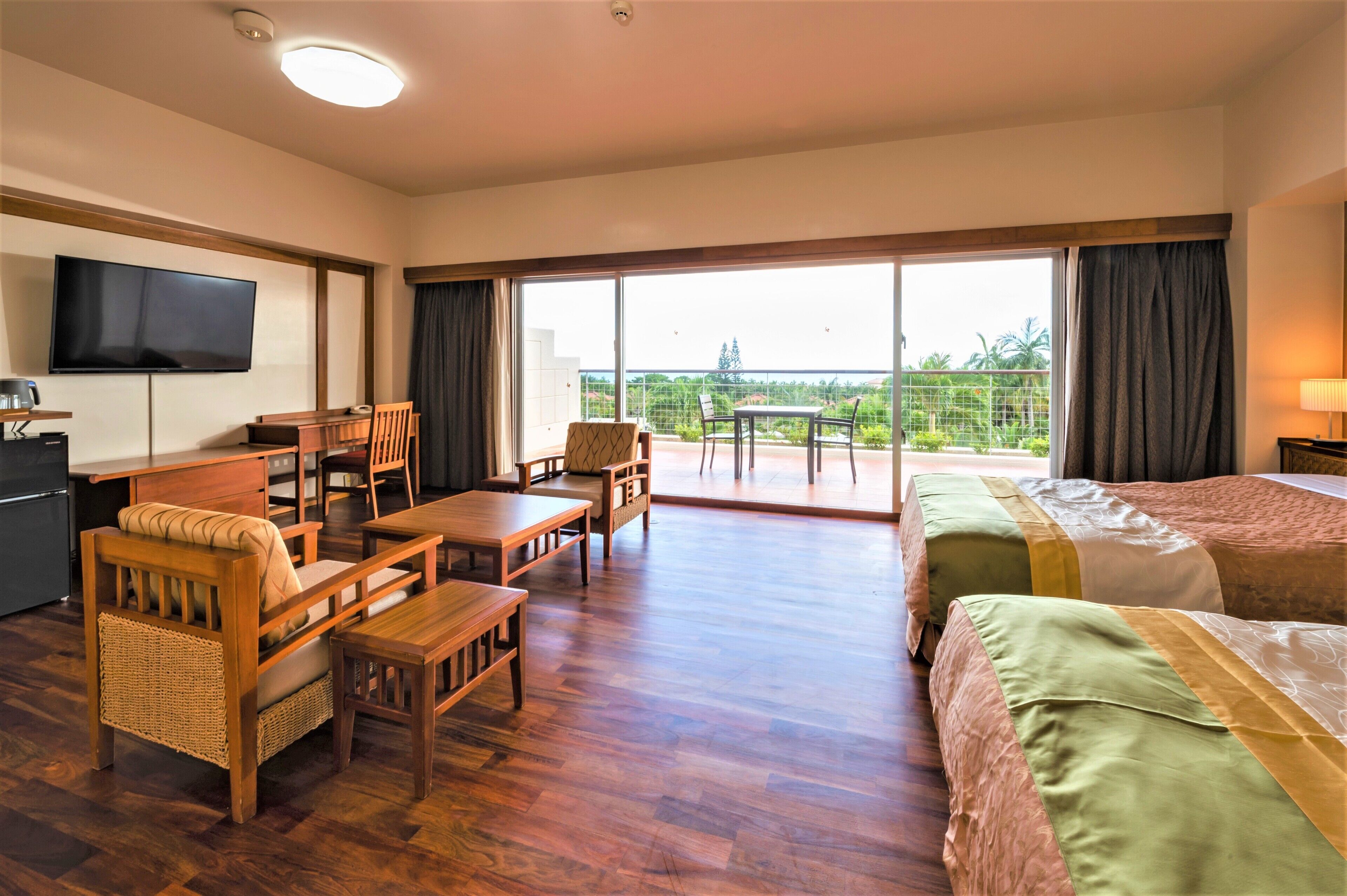 Quarto de hotel com chão de madeira, televisão fixada na parede, área de refeições com mesa e cadeiras e varanda com vista.