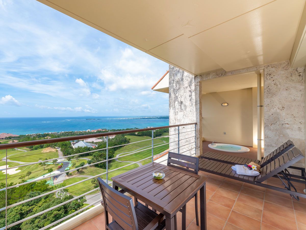 Un balcon avec une table et des chaises, un petit jacuzzi et une vue sur un terrain de golf et l’océan.