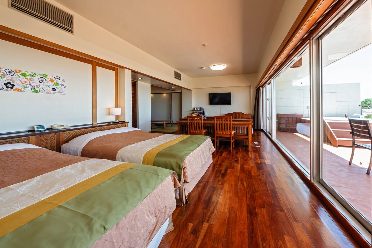 A hotel room with two beds, a dining area, and a large window offering a view.