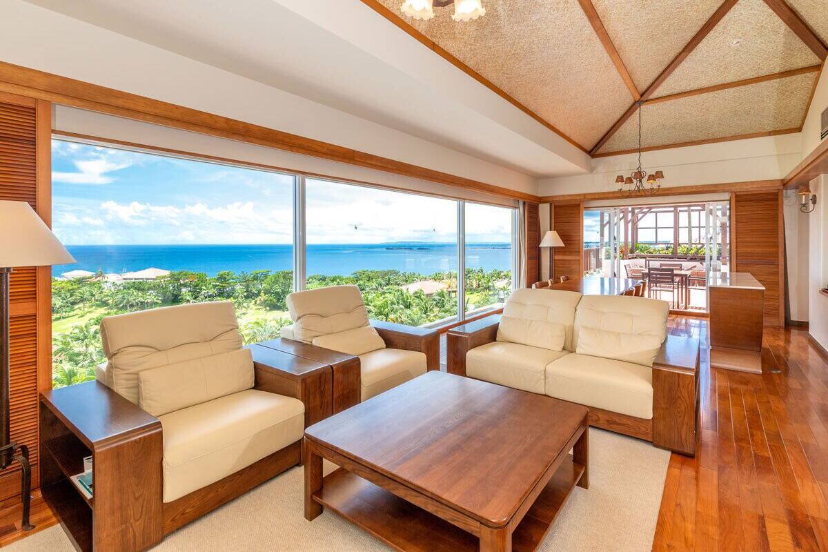A spacious living room with large windows offering a view of the ocean. There are two sofas and a coffee table.