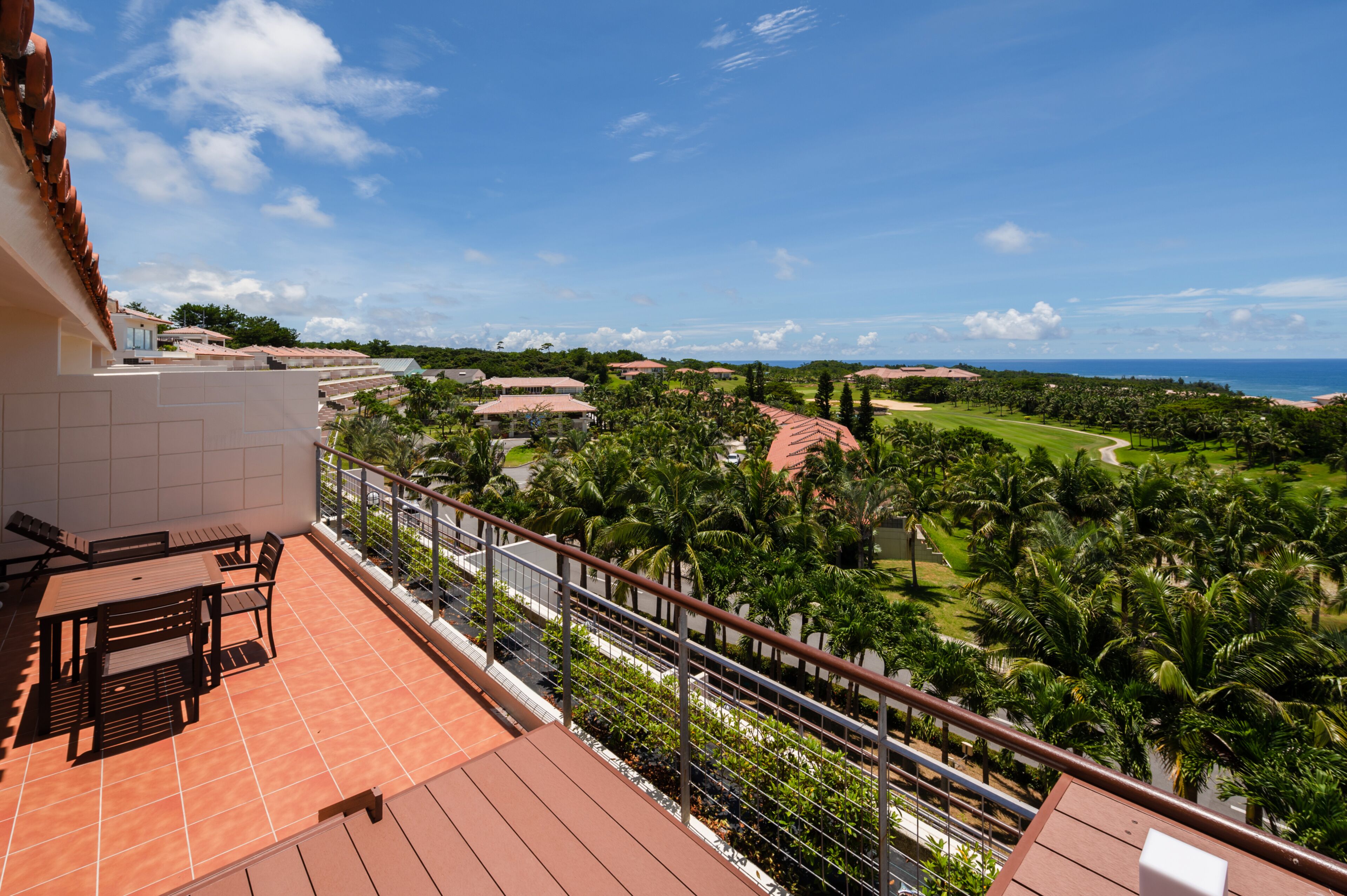 A balcony with a table and chairs, overlooking a golf course and ocean.
