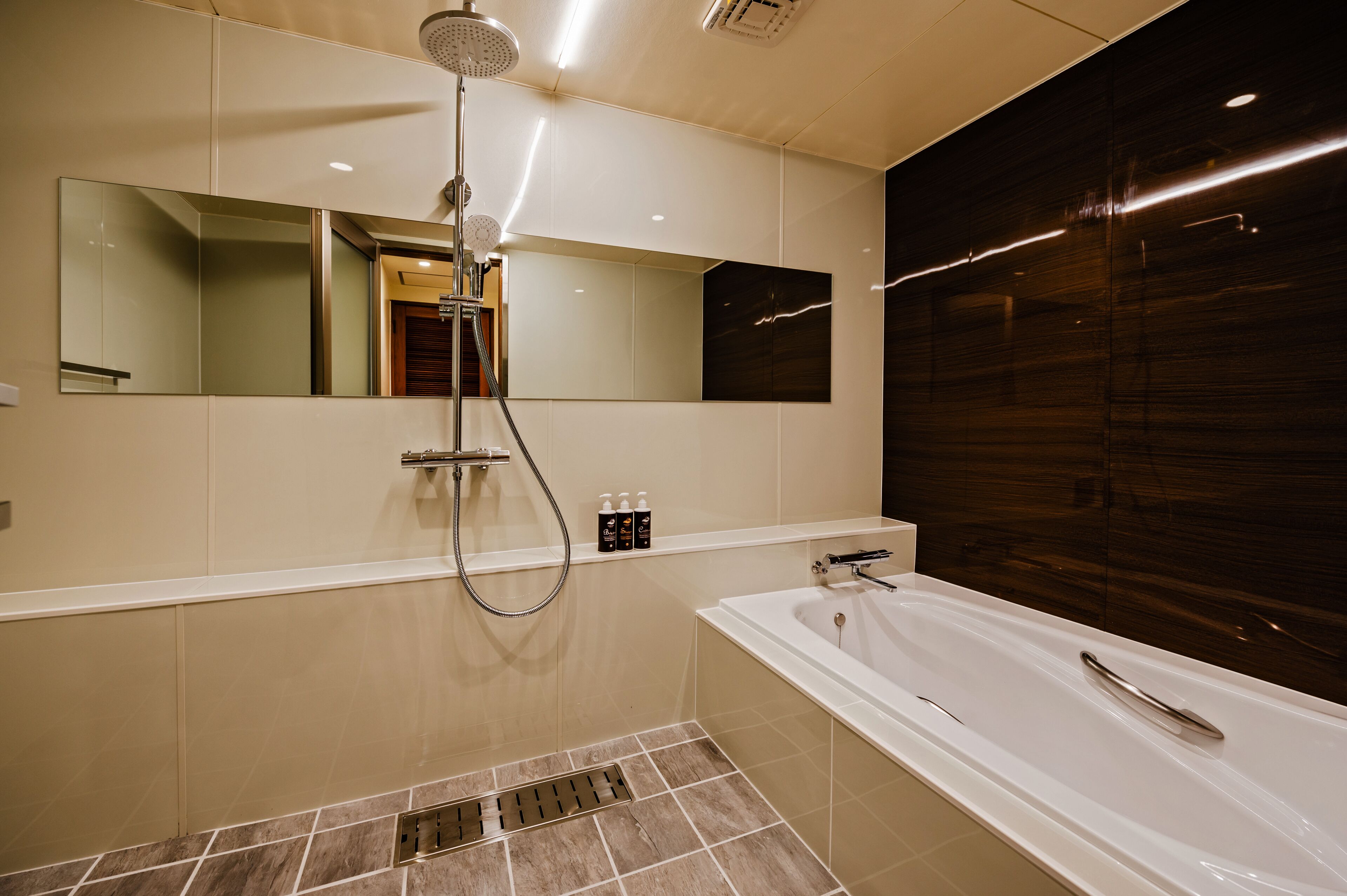 Un baño moderno con un espejo grande, una ducha, una bañera y un tocador con artículos de aseo.