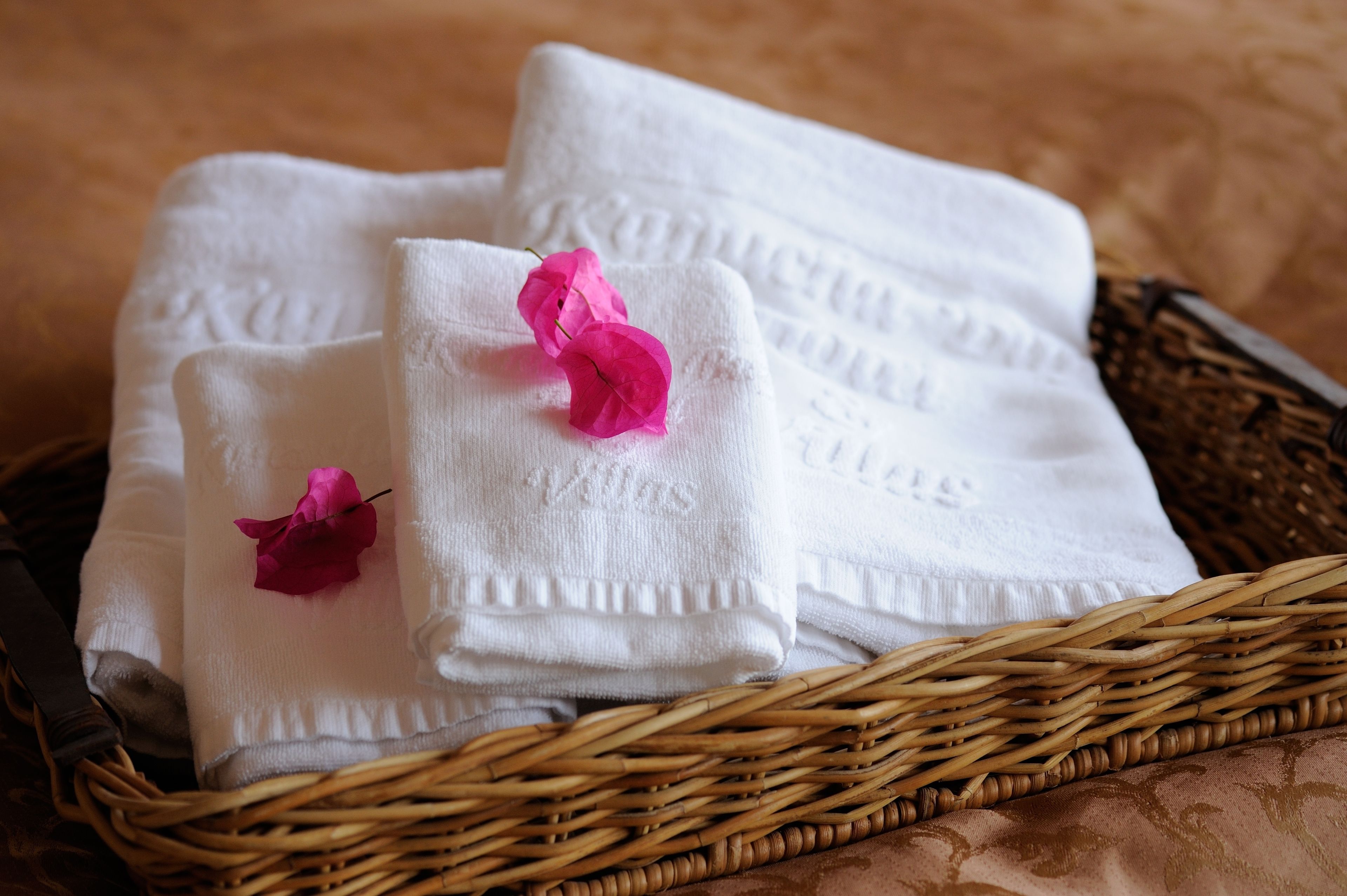 A wicker basket containing neatly folded white towels with embossed text and a pink flower.