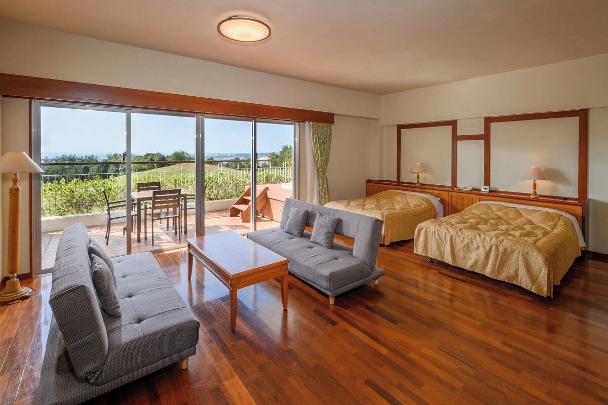 A hotel room with a balcony, a sofa, a bed, and a wooden floor.