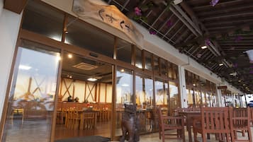 Un restaurante con mobiliario de madera, un amplio acceso de vidrio y flores colgantes.