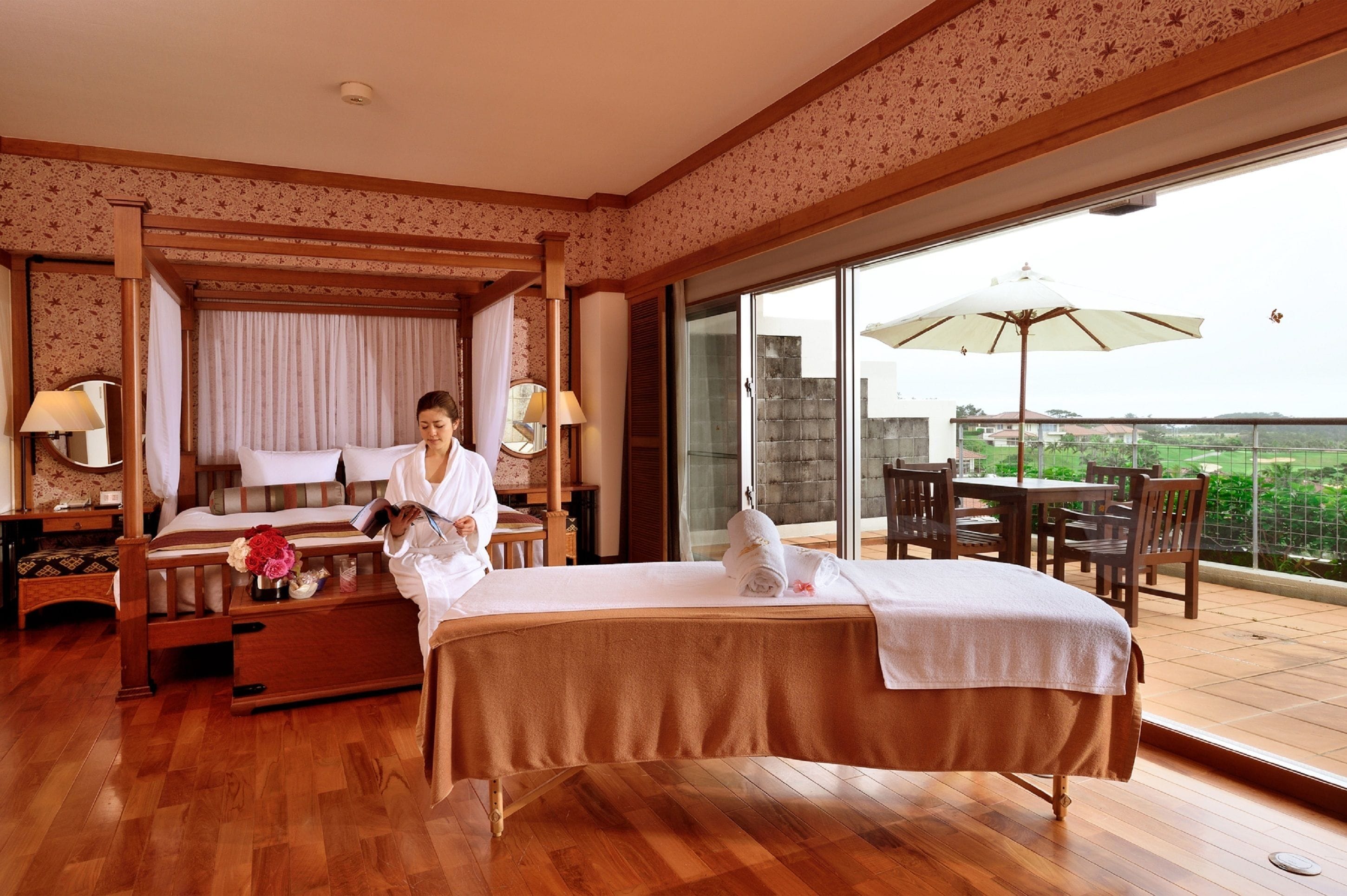 Habitación de hotel con una cama grande, un área de descanso con mesa y sillas, y un balcón con sombrilla.