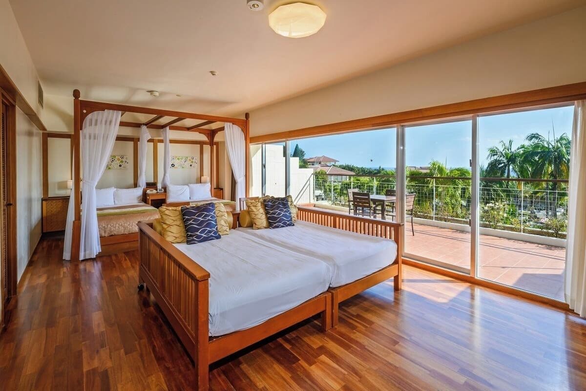 A spacious bedroom with a large bed, a canopy bed, and a balcony with a view of palm trees.