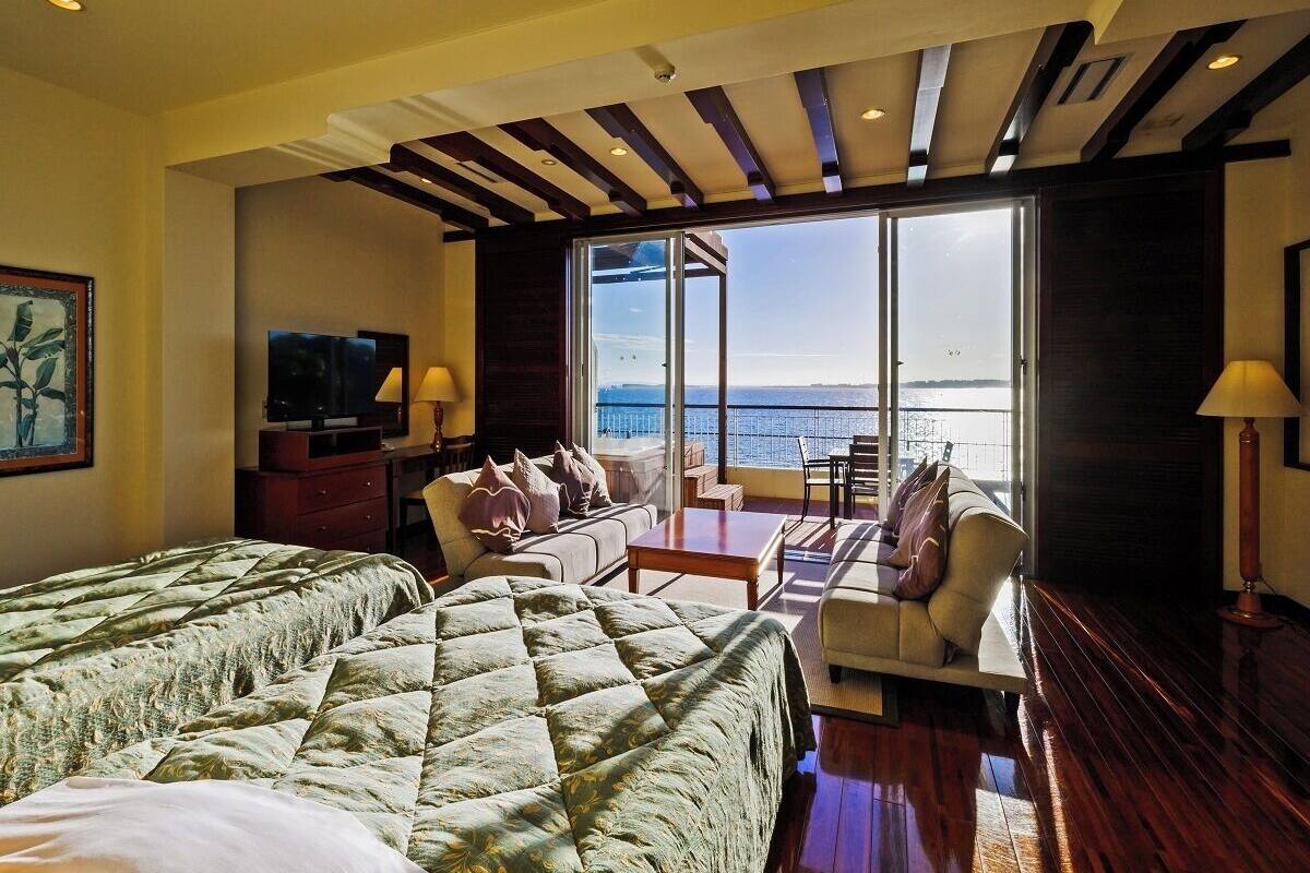 A hotel room with two beds, a sofa, a small table, and a view of the sea.