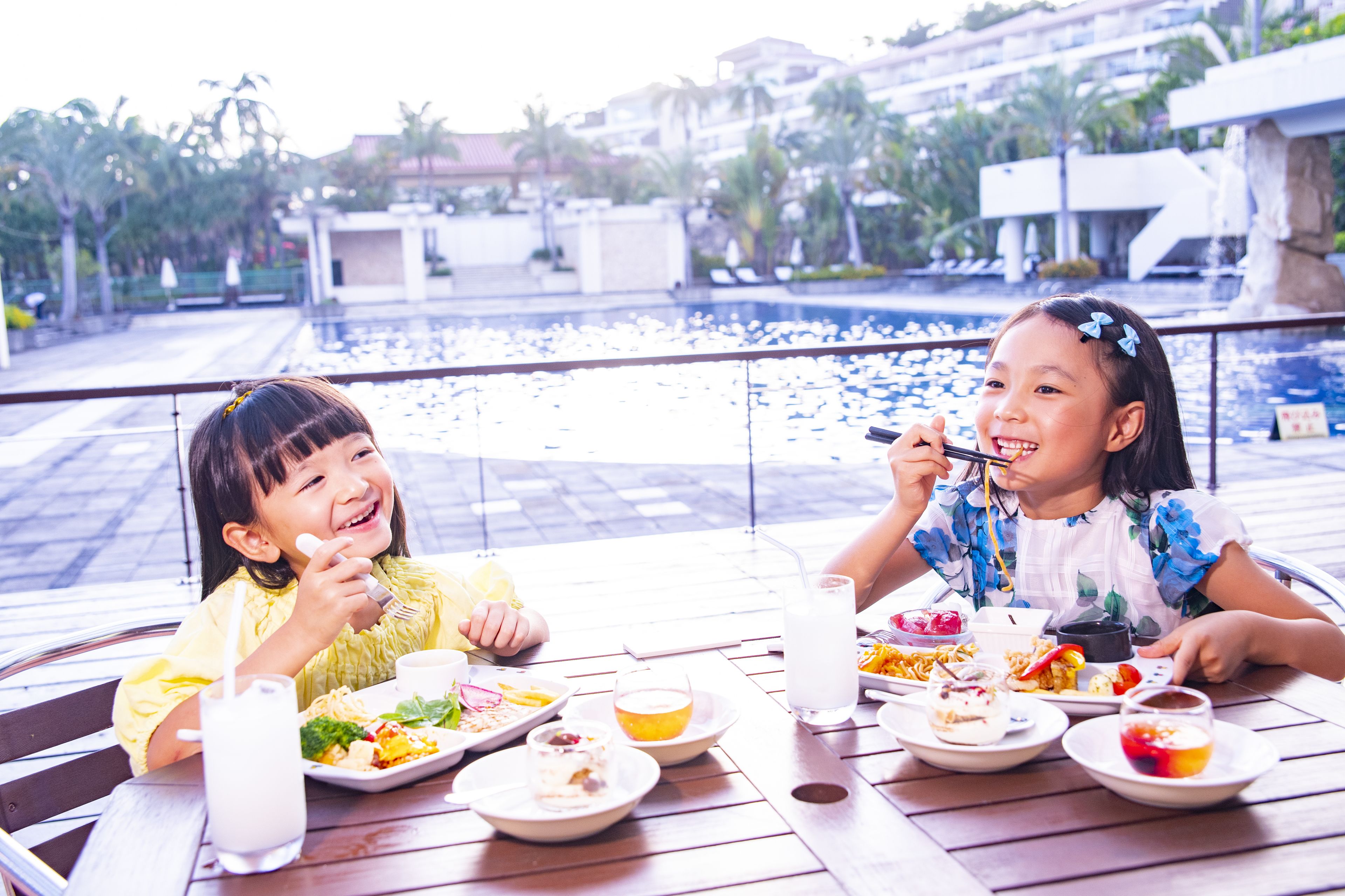 Two people dining at an outdoor table with a view of a pool and buildings in the background.