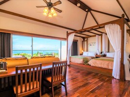 A room with a bed, a dining table, and a view of the ocean.