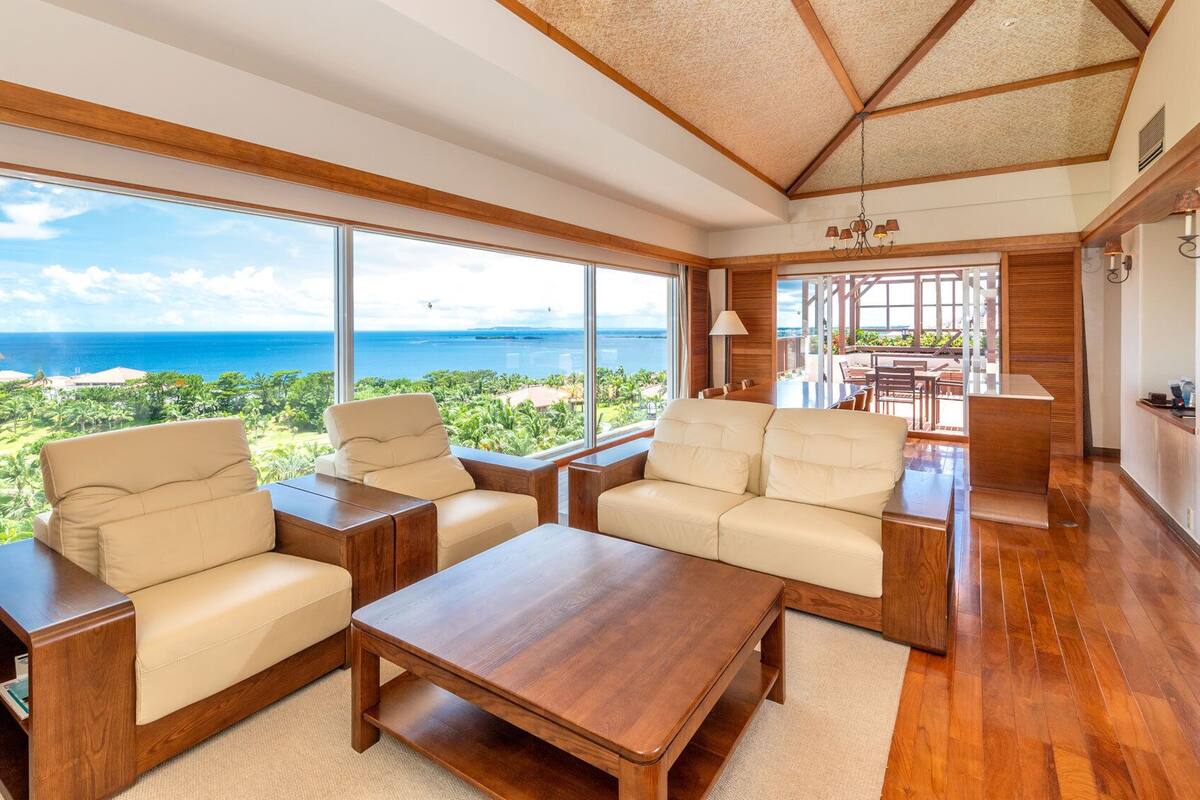 A spacious living area with large windows, wooden furniture, and a view of the ocean.