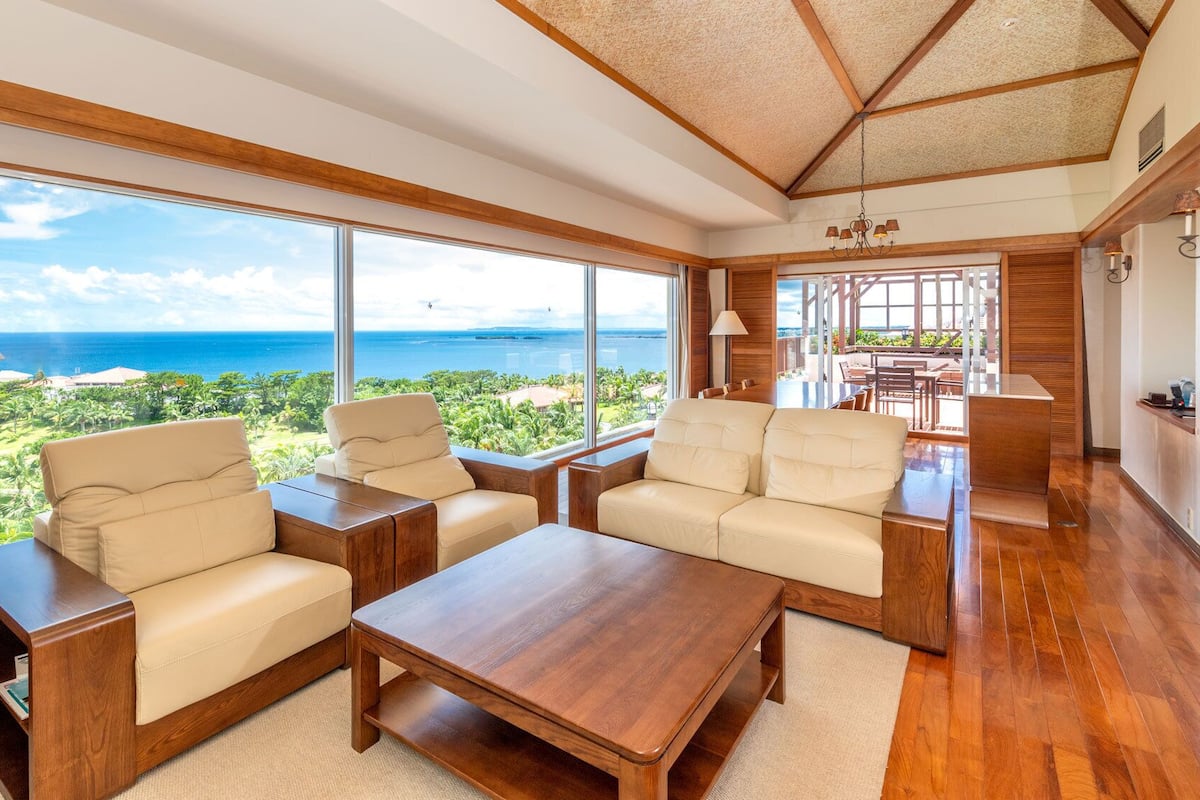 A spacious living area with large windows, wooden furniture, and a view of the ocean.